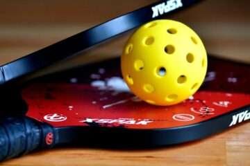 yellow color pickleball ball held between two paddles