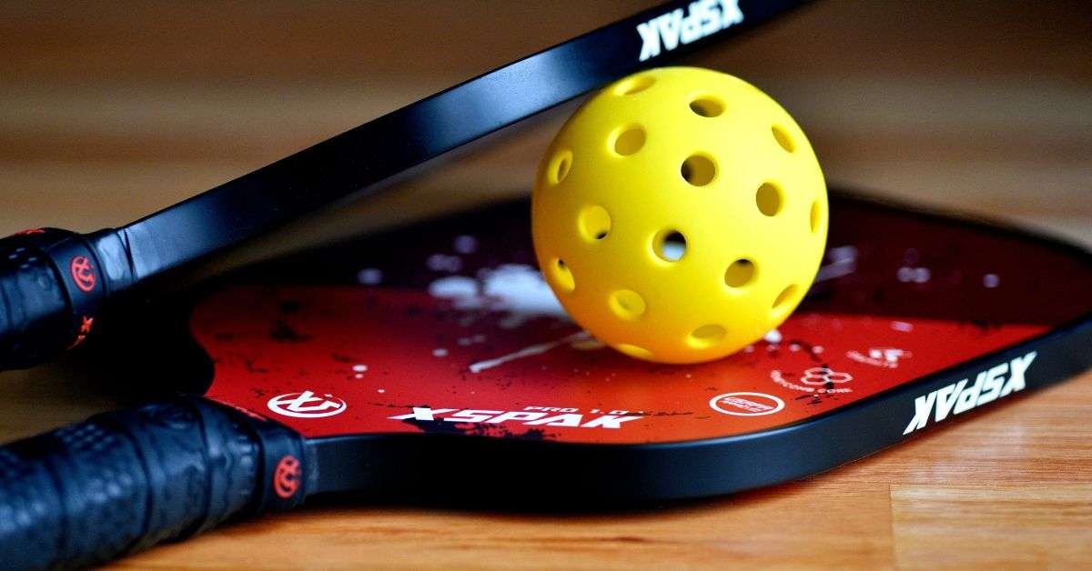 yellow color pickleball ball held between two paddles